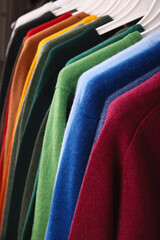Warm sweaters. Autumn, winter clothes. Metal rack with various sweaters on hangers placed in modern...