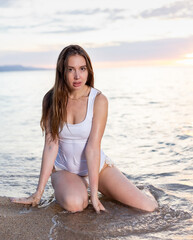 Fototapeta na wymiar Sexy girl sitting at sand at sea shore at sunset