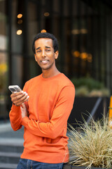 Handsome smiling African American man businessman holding mobile phone, checking mail looking at camera outdoors. Technology concept