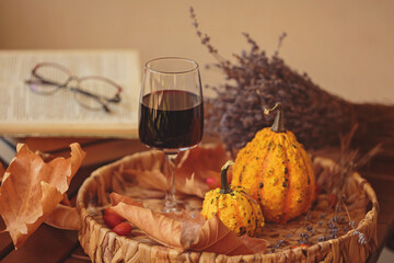 Glass of red wine on wooden table decorated with pumpkins, books and dried leaves outdoor. Autumn...