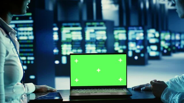 Tech savvy admins running code on chroma key laptop, troubleshooting data center equipment. Specialists using mockup device to monitor servers, networking systems and storage arrays