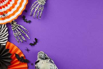 Grasping the mysterious enchantment interwoven with Halloween. Top view composition of skull, skeleton hands, paper party props, creepy decor on purple background with marketing space
