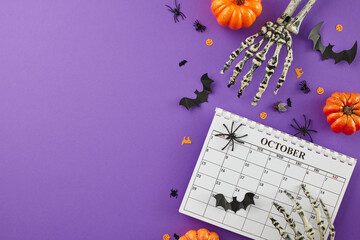 The ghostly vibes resonating with the Halloween spirit in October. Top view of calendar, skeleton hands, pumpkins, scary decor on purple background with ad placement