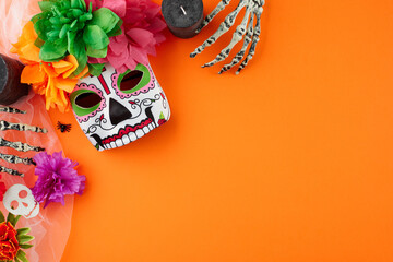 Immerse yourself in vibrant day of the dead festivities. Top view photo of traditional mask, skeleton hands, skulls, candles, flowers, scary decor on orange background with ad space