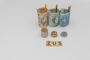 Banknotes arranged in a roll with 3 denominations of 50 zloty 100 zloty and 200 zloty next to which lie coins and zus wood inscription. The concept of early retirement, increasing the value of contrib