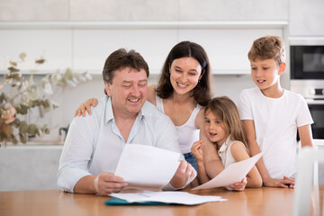 Obraz premium Happy satisfied family reading documents together while sitting at the table at home