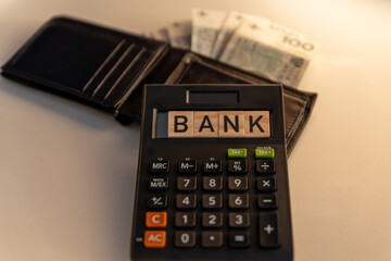 A wallet with banknotes lying next to a calculator with a Bank sign. The concept of spending during a recessionary crisis.
