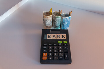 Banknotes stacked in a roll of 3 denominations of 50 zloty 100 and 200 zloty next to which lies the Bank's wood sign on a calculator. The concept of spending during the recession crisis. 