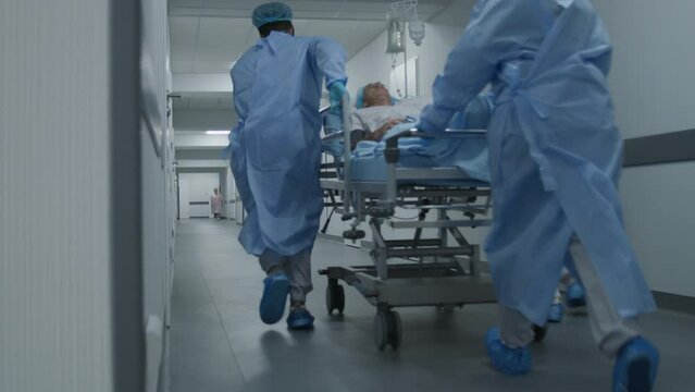 Doctors, nurses and paramedics run and push stretcher with seriously injured patient to surgery room. Medical personnel save human life in emergency department. Medical facility hallway. Slow motion.