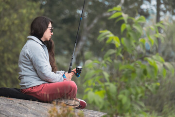 alone woman waiting to catch a fish holding her fishing rod in the forest