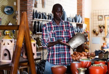 Portrait of welcoming Afro male seller in pottery souvenir shop - obrazy, fototapety, plakaty