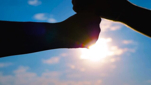 Close up: silhouettes of man and woman hands are bumping fists against the sunset or sunrise sky - sun lens flares. Informal greeting, giving dap, agreement, friendship and teamwork concept