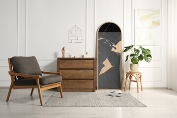 Broken mirror, wooden chest of drawers, armchair and houseplant in room
