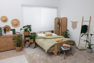 Stylish bedroom with comfortable bed and beautiful green houseplants. Interior design