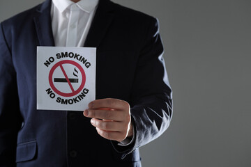 Man holding card with no smoking sign on gray background, closeup. Space for text