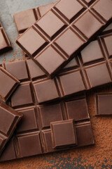 Delicious dark chocolate and cocoa powder on black table, flat lay