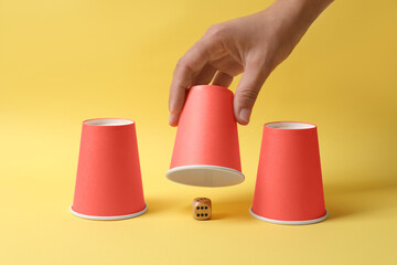 Woman showing dice under cup on yellow background, closeup. Thimblerig game
