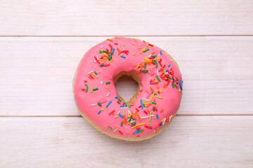 Glazed donut decorated with sprinkles on white wooden table, top view. Tasty confectionery