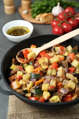 Delicious ratatouille and spoon in baking dish on table, closeup