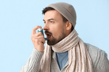 Ill young man with inhaler on blue background, closeup