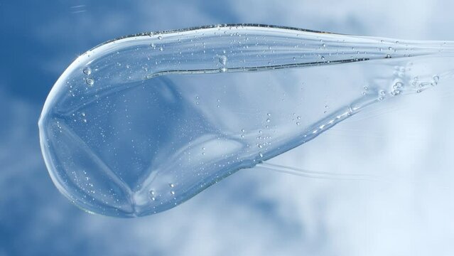 Female hand using spatula applies smear of shampoo or shower gel against the background of sky and clouds, top view.