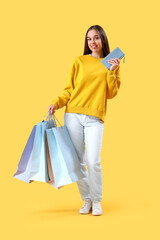 Young woman with wallet and shopping bags on yellow background