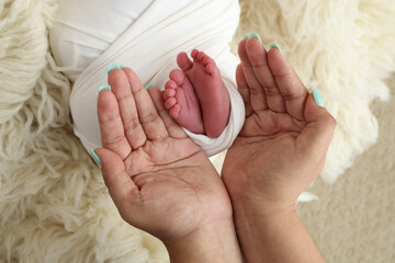 The palms of the father and mother are holding the foot of the newborn baby in a white blanket. 