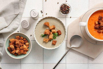 Pot and bowl of tasty cream soup with croutons on white tile background