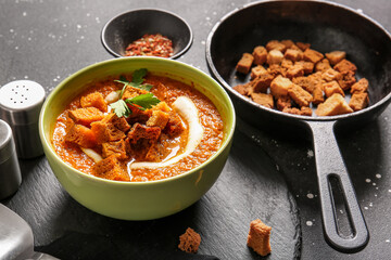 Bowl of tasty cream soup with croutons on black background