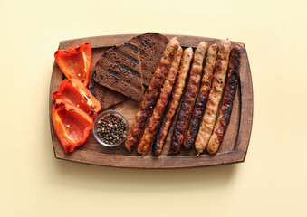 Wooden board of tasty grilled sausages with bread and bell pepper on yellow background