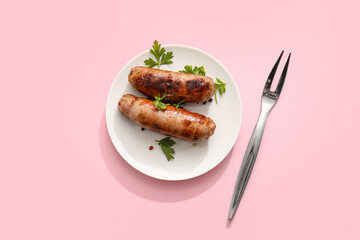Plate of tasty grilled sausages and fork on pink background