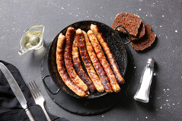 Frying pan of tasty grilled sausages and bread on black background