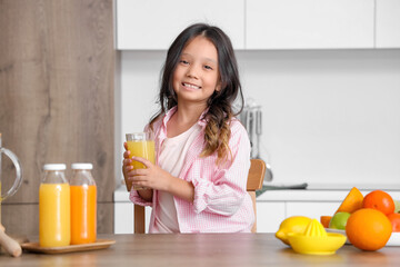 Little Asian girl with fresh juice and plate of different citruses at table in kitchen