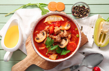Bowl of tasty beef stew and ingredients on green wooden background