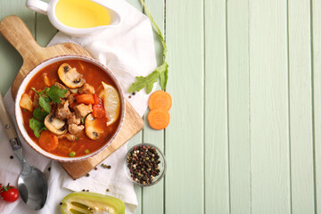 Bowl of tasty beef stew and ingredients on green wooden background