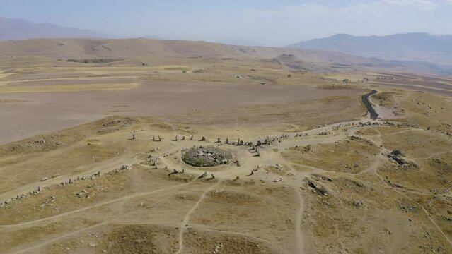 Backward reveal aerial shot of Zorats Karer (Carahunge or Armenian Stonehenge) on sunny summer day. Sisian, Armenia.