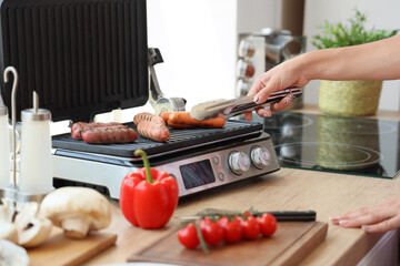 Woman cooking delicious sausages on modern electric grill in kitchen, closeup
