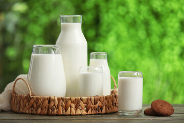 Glasses and bottles of fresh milk with sweet cookies on wooden table outdoors
