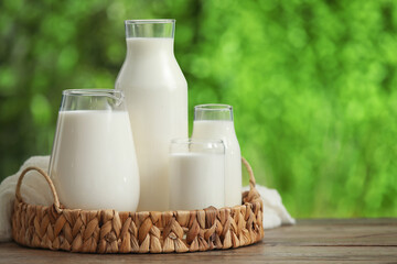 Jug and bottles of fresh milk on wooden table outdoors