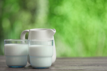 Glasses and jug of fresh milk on wooden table outdoors