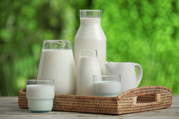 Glasses and bottles of fresh milk on white wooden table outdoors