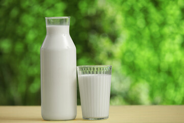 Glass and bottle of fresh milk on yellow wooden table outdoors