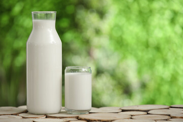 Glass and bottle of fresh milk on wooden table outdoors