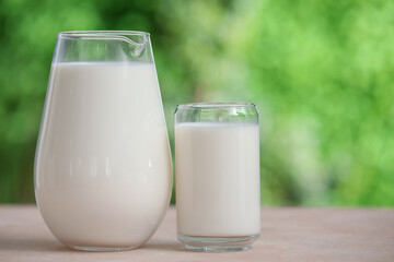 Glass and jug of fresh milk on beige table outdoors