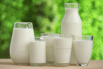 Glasses and jug of fresh milk on beige table outdoors
