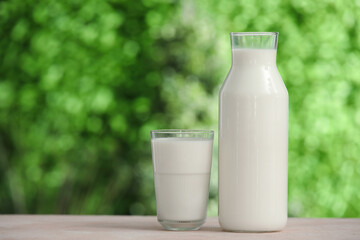 Glass and bottle of fresh milk on beige table outdoors