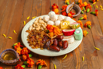 Diya lamps with marigold flowers and plate of treats on brown wooden background. Divaly celebration