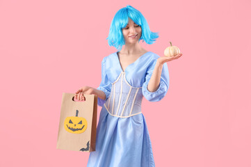 Young woman dressed for Halloween with gift bag and pumpkin on pink background