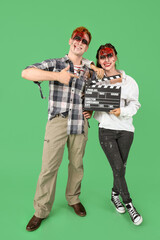 Fototapeta premium Young couple dressed for Halloween as zombies with movie clapper on green background