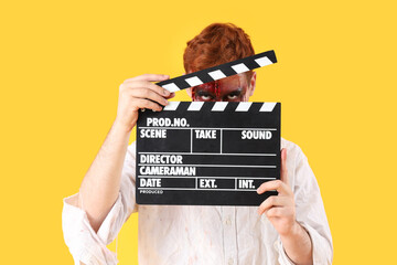 Young man dressed for Halloween as zombie with movie clapper on yellow background